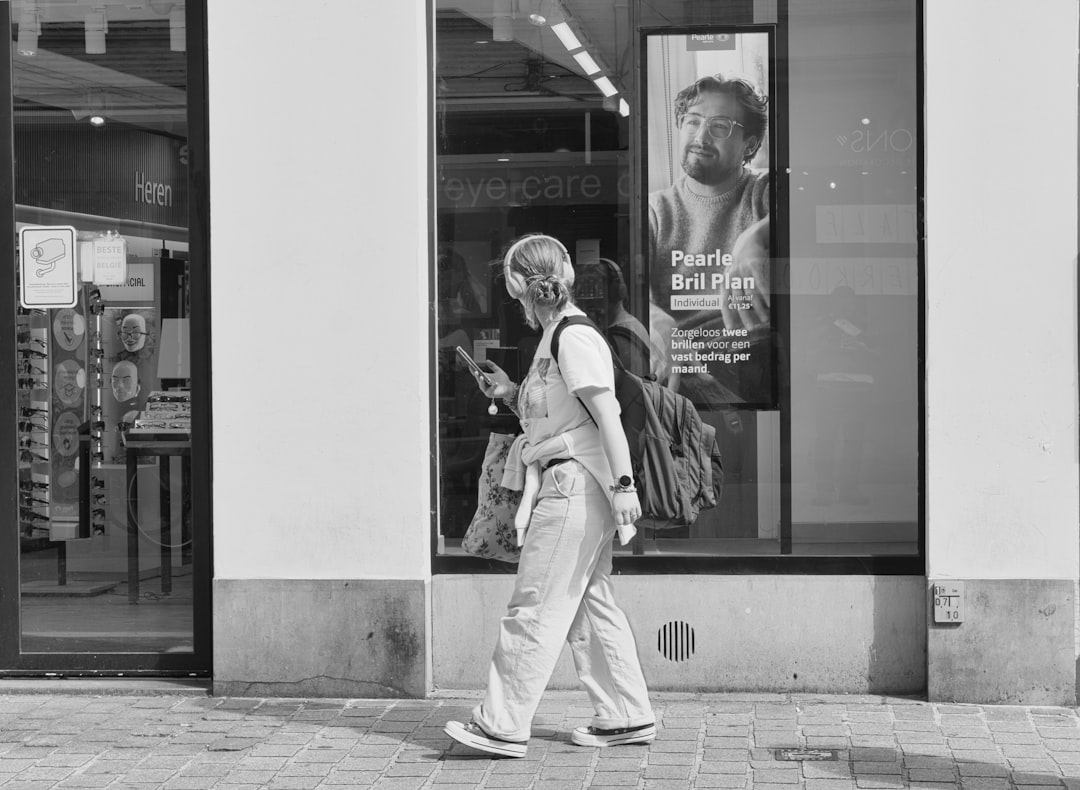 Woman wearing headphones walks past storefront with advertisement